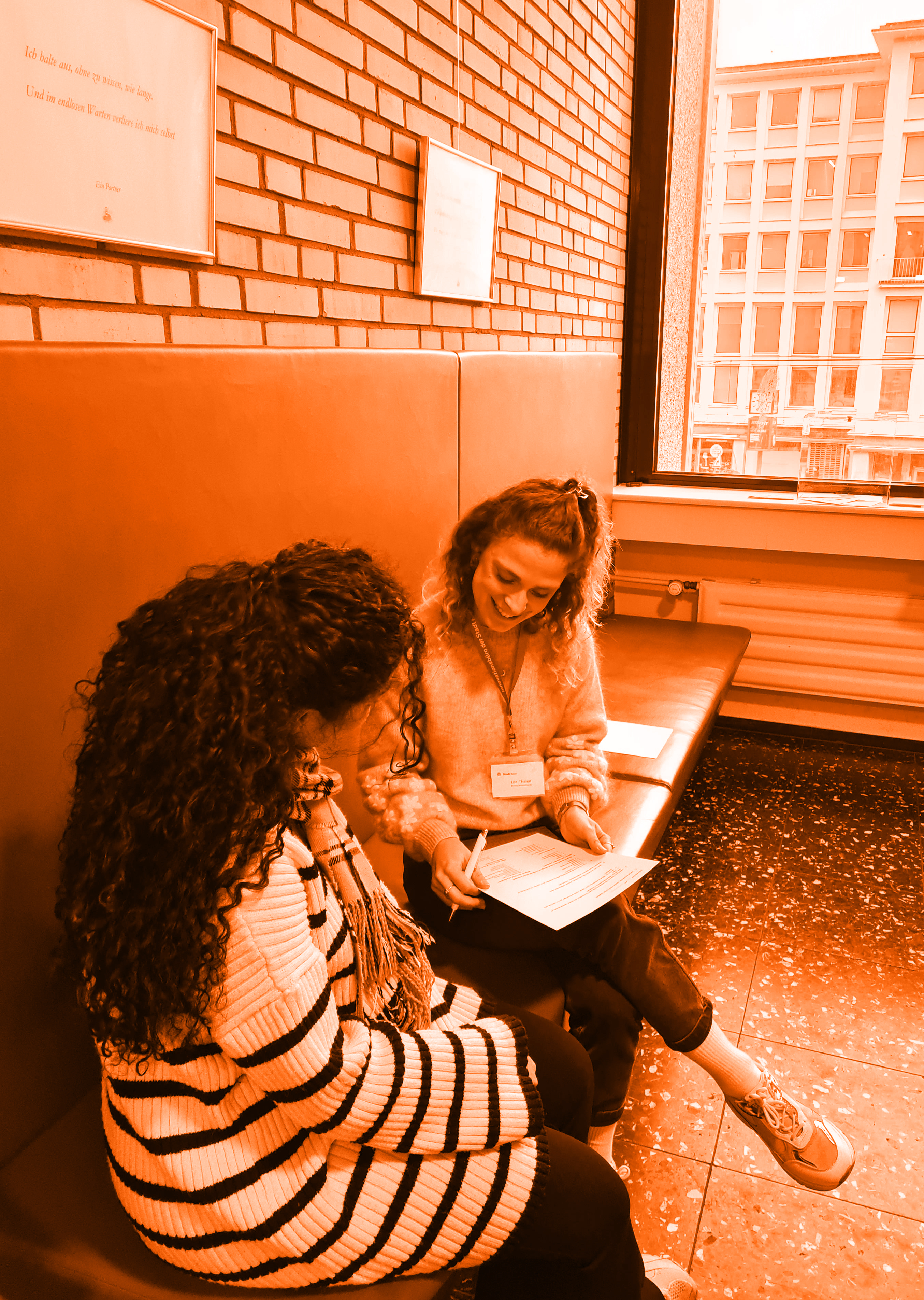 Foto von zwei Frauen, die auf einer Bank sitzen unten sich über einen Fragebogen unterhalten